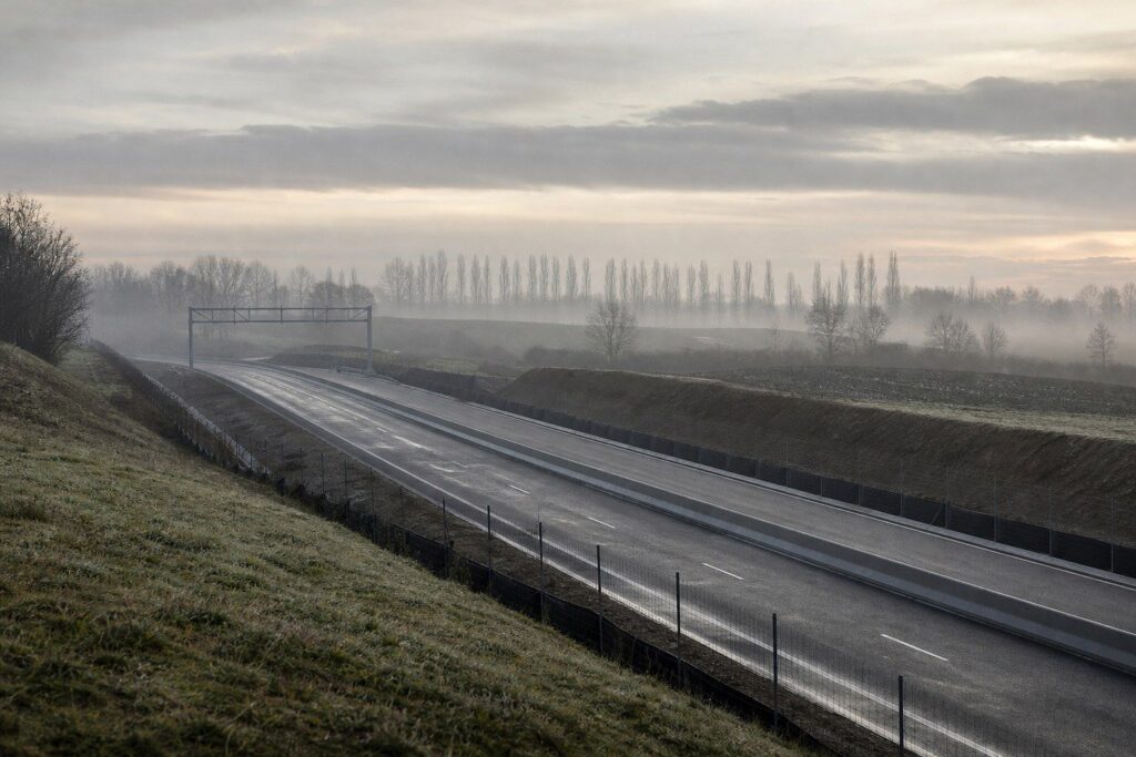 Route déserte bordée de barrières de sécurité, arbres dénudés sous un ciel gris brumeux