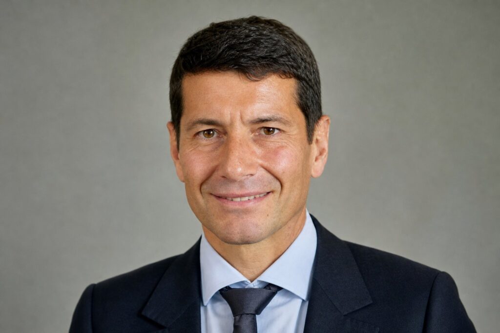 Portrait en buste d'un homme politique, cheveux courts bruns, costume sombre, arrière-plan neutre flou.