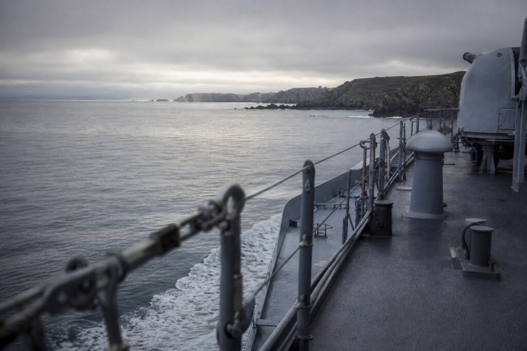 Pont d'un navire militaire en mer, côte rocheuse à l'horizon sous un ciel nuageux
