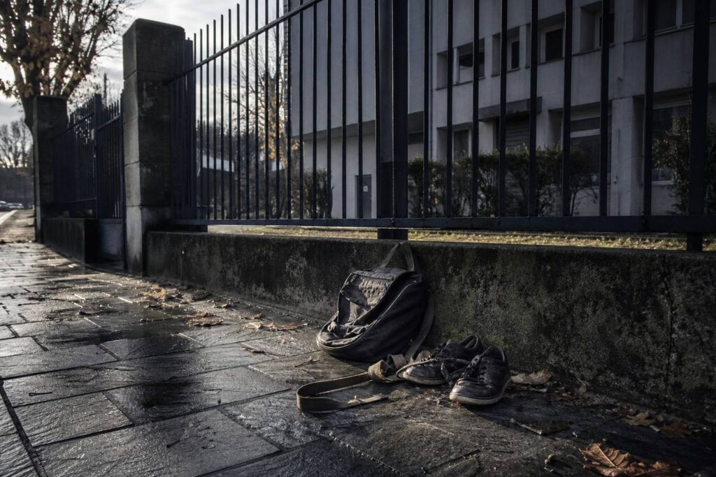 Trottoir humide, feuilles mortes, sac à dos et chaussures usées contre un muret