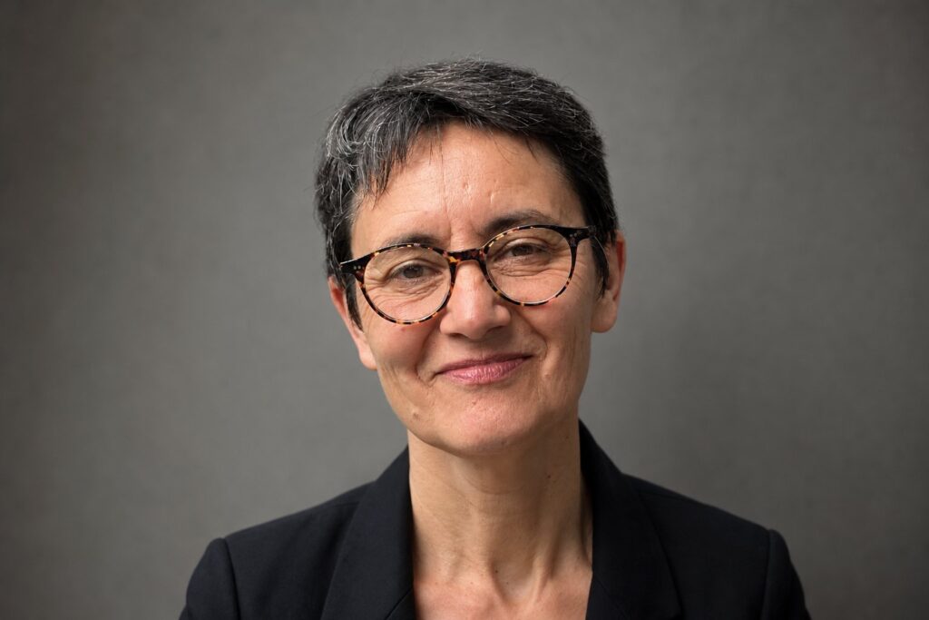 Femme en buste portant des lunettes, cheveux courts gris, sur fond neutre flou.